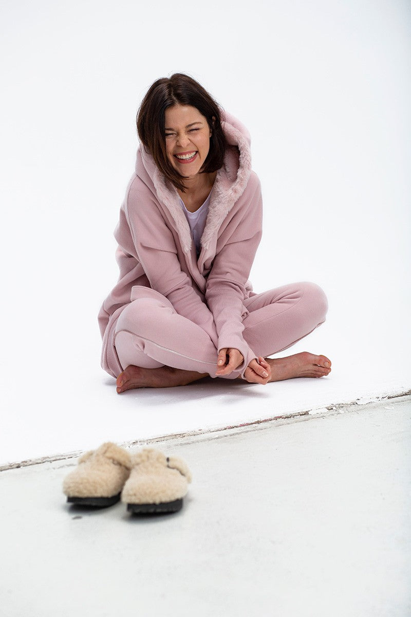 Kobieta w różowym, wygodnym dresie z kapturem, siedząca na podłodze – self-care fashion