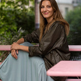 Kobieta w eleganckiej sukience i kurtce, siedząca na różowej ławce w zielonym ogrodzie – moda polska, self-care fashion