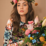 Kobieta w kwiecistej sukience z wiankiem kwiatów, trzymająca bukiet róż i lilii – moda polska, self-care fashion