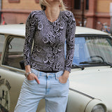 Kobieta w czarno-białej bluzce z kwiatowym wzorem i jasnych jeansach, uśmiechnięta, oparta o retro auto