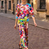 Kobieta w kolorowej, graficznej sukience z motywem lalek, spacerująca po brukowanej ulicy. Moda polska, self-care fashion.
