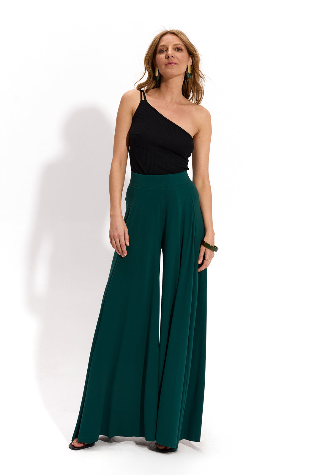 Kobieta w zielonych spodniach wide leg i czarnej bluzce jednoremieniowej, stylowa i wygodna moda